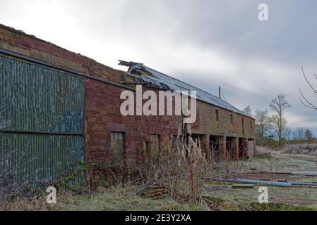 Ein zerstörter Stein Farm Barn mit dem Schieferdach eingefallen, und Teile der Ausrüstung liegen auf dem Hartstand neben den Maschinenhallen. Stockfoto