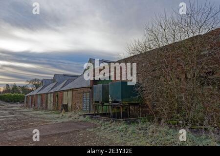 Ein ruiniertes Farmgebäude oder Landwirtschaftsladen mit zwei leeren Treibstofftanks neben einer der Steinmauern neben einer Metallschiebetür. Stockfoto