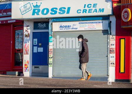 Southend on Sea, Essex, Großbritannien. Januar 2021. Der heftige Regen des Sturms Christoph hat durch die Küstenstadt zu einem sonnigen Tag geblasen. Die Leute trainieren und arbeiten an den Strandpromenaden. Person, die an geschlossenen Rossi-Eisdielen am Meer vorbeikommt Stockfoto