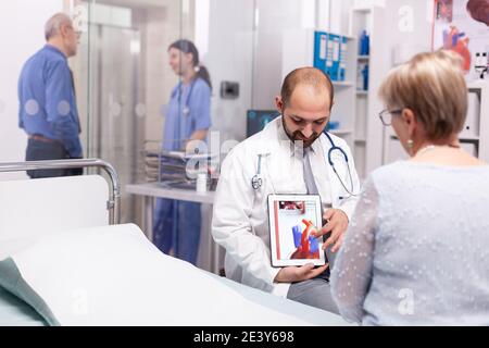 Arzt erklärt Behandlung für Herzerkrankungen an ältere Frau im Sprechzimmer. Kardiologe mit Stethoskop, der mit dem Patienten über eine ungesunde Herzerkrankung spricht. Stockfoto
