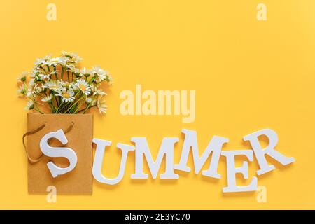 Text SOMMER aus weißen Volumen Buchstaben und Feld chamomies Blumen in Handwerk Paket auf gelbem Hintergrund. Grußkarte Flat Lay Kopierraum Konzept He Stockfoto