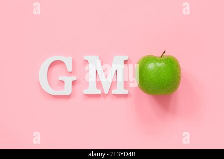 GMO tex aus weißen Volumen Buchstaben und grünen Apfel auf rosa Hintergrund. Konzept von genetisch veränderten Lebensmitteln oder Früchten. Draufsicht Flat Lay Copy Space. Stockfoto