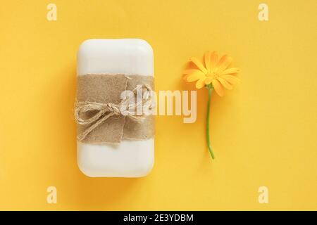 Handgemachte Naturseife mit Bastelpapier, Geißel und orangefarbenen Ringelblumen auf gelbem Hintergrund verziert. Bio-Kosmetik-Konzept. Draufsicht flach Stockfoto