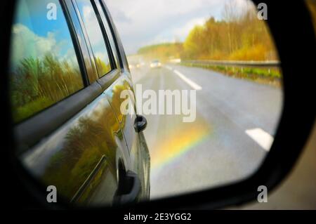 Verschwommener Regenbogen (nach Regen), der im Autospiegel reflektiert wird. Abstrakter Hintergrund für Reisen. Stockfoto