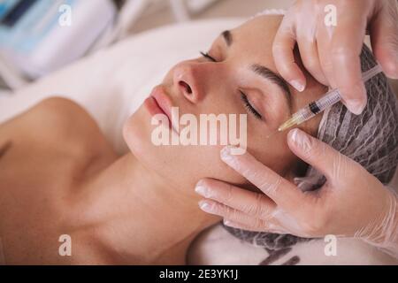 Wunderschöne junge Frau erhalten verjüngende Gesichts-Injektionen in Beauty-Klinik. Kosmetologe injiziert Gesichtsfüller in die Haut eines Kunden Stockfoto