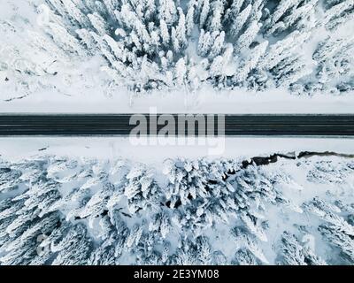 Highway, der durch einen gefrorenen, schneebedeckten Wald führt. Vogelperspektive. Stockfoto