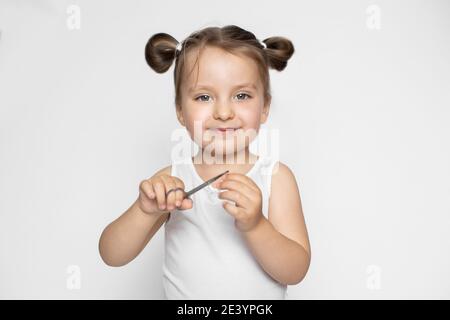 Ein kleines Mädchen mit blonden Haaren in zwei Pferdeschwänzen, posiert vor der Kamera mit glücklichen Lächeln auf isolierten Studio weißen Hintergrund, während die Maniküre Stockfoto