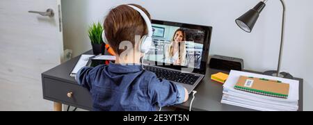 Unerkennbarer Junge mit Kopfhörern, der zu Hause mit einem Laptop von seinem Schlafzimmer aus Unterricht erhält. Home Schulkonzept Stockfoto