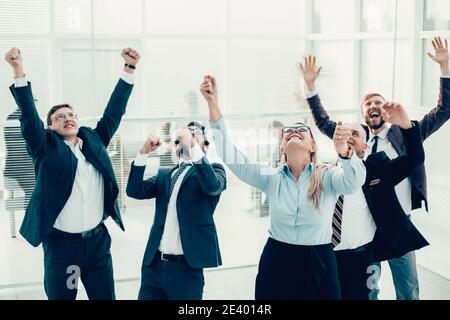 Glückliche Geschäftsfrau, die vor einem jubelnden Geschäftsteam steht. Stockfoto