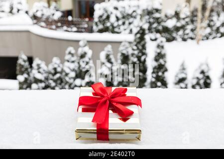 Ein Weihnachtsgeschenk in einem festlichen Paket liegt auf dem Schnee. Weihnachtstraditionen des Austausches von Geschenken. Stockfoto
