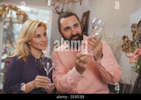 Glücklich schöne Frau genießen Einkaufen für Glaswaren mit ihrem schönen Mann. Reifes Ehepaar, das Weingläser beim Einkaufen zusammen checkt Stockfoto