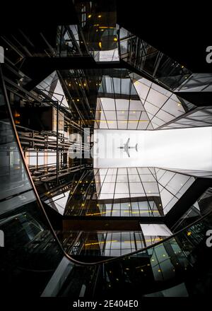 Jumbo Jet Fracht Passagierflugzeug fliegen über moderne Architektur Glas Reflection Sky Scraper Gebäude im Stadtzentrum dramatische Aussichtspunkt symmetrisch Stockfoto