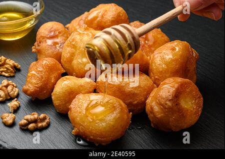 Hausgemachte Lokma serviert mit Honig, Nüssen und Zimt auf schwarzem Gericht Stockfoto