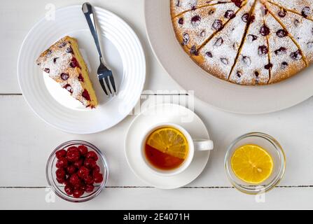 Draufsicht Nahaufnahme von Kirschkuchen in Scheiben, Stück Kuchen auf einem Teller und Zitronentee. Selektiver Fokus, horizontale Ausrichtung. Stockfoto