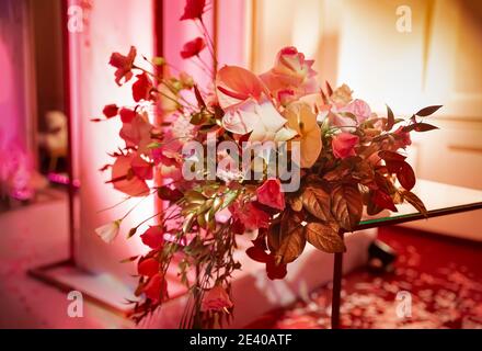 Ein luxuriöser Strauß aus bunten Rosen und verschiedenen Blumen auf einem Glastisch in rosa Licht bei der Feier. Blumenstrauß zum Valentinstag, Heiratsfest Stockfoto