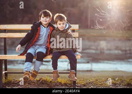 Zwei niedliche Jungen, Brüder, sitzen auf einer Bank, liebevoll miteinander. Speicherplatz kopieren Stockfoto