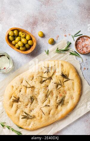 Frisch gebackenes italienisches traditionelles hausgemachtes Focaccia-Brot mit Gewürzen und Rosmarin auf Pergamentpapier und hellgrauem Hintergrund. Draufsicht. Stockfoto