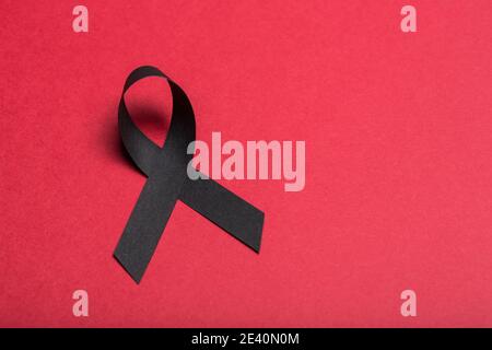 Schwarzes handgemachtes Awareness Papierband auf rotem Hintergrund. Stockfoto