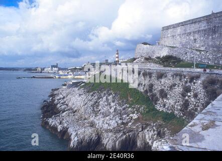 1985 Plymouth Hoe - Blick auf den Smeatons Tower von Madeira an der Königlichen Zitadelle vorbei, eine Festung aus dem 17th. Jahrhundert mit barockem Tor, einer Garnisonkirche und historischen Waffen. Es beherbergt jetzt die Marine Biological Association auf dem Hügel der Zitadelle. Der Smeatons Tower ist ein rot-weiß gestreifter Leuchtturm aus dem 18th. Jahrhundert mit Blick auf den Plymouth Sound, der einst das Eddystone Riff markierte, Tinside Lido ist 1935 zu sehen und erbaut, das lido im Art-Deco-Stil und Grade II in Plymouth Devon England GB UK Europe gelistet Stockfoto