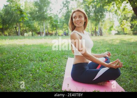 Fröhliche schöne Frau bewundern die Natur, tun Yoga im Park auf Gras, kopieren Raum. Schöne rothaarige Frau Yoga praktizieren, sitzen in Lotus-Position Stockfoto
