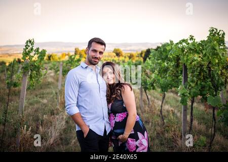 Glückliches junges Paar erwartet Baby. Mann umarmt seine schwangere Frau im Freien. Gutaussehende verheiratete Menschen Stockfoto