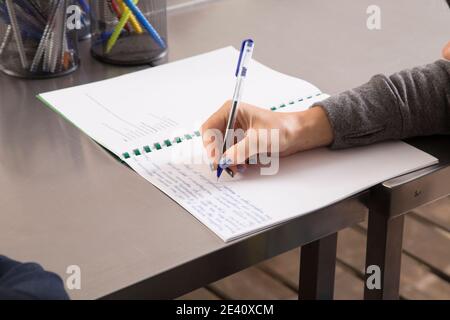 Eine Frau schreibt in der Meisterklasse ein Rezept. Notizbuch für Rezepte steht auf einem Metalltisch aus Edelstahl. Nahaufnahme. Stockfoto