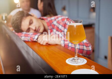 Selektive Konzentration auf ein Glas Bier an der Theke, junger Mann schläft betrunken in der Kneipe Stockfoto