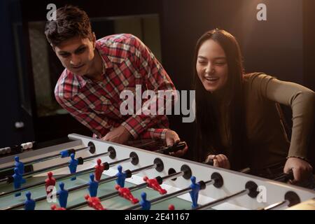 Junges Paar spielt Tisch footbal auf einem Datum. Attraktive Mann und seine schöne asiatische Freundin mit Spaß zusammen, spielen Tischfußball Stockfoto