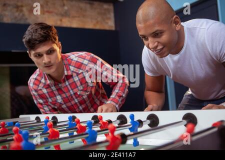 Zwei junge männliche Freunde spielen Tischfußball. Schöner afrikanischer Mann, der mit seinem Freund Tischfußball spielt Stockfoto