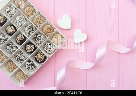 Schokolade handgemachte Bonbons auf rosa Holztisch. Schokoladenbox offen mit zwei Herzen und einem festlichen Band. Geschenk zum valentinstag Stockfoto