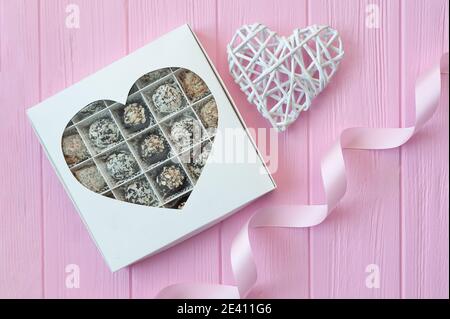 Schokolade handgemachte Bonbons auf rosa Holztisch. Schokoladenbox mit Herz und einem festlichen Band. Geschenk zum valentinstag Stockfoto