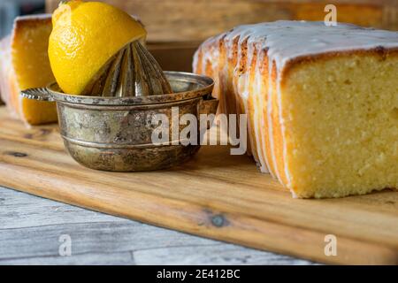 Köstliche Zitronenkuchen mit Zuckerguss auf Holzbrett mit rustikalen Küchenutensilien Stockfoto