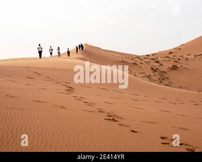 Eine Reihe von Touristen klettern eine große Sanddüne in Merzouga, Sahara von Marokko. Stockfoto