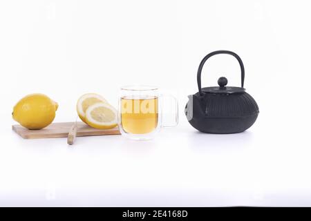 Transparente Tasse mit grünem Tee, schwarzer Teekanne und Zitrone isoliert auf weißem Hintergrund Stockfoto