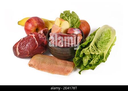 Hundeschale gefüllt mit biologisch geeigneten Rohkost mit Fleischstückchen, Fisch, Obst und Gemüse, umgeben von Zutaten auf weißem Backgrou Stockfoto