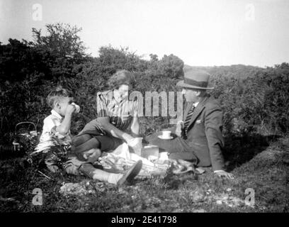 Eine Mutter, Vater und ihr Sohn sitzen glücklich auf dem Land bei einem Picknick und genießen das Leben im Freien in der 1940s Stockfoto