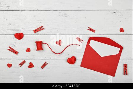 Vorbereitung Valentine Geschenke, rote Herzen, Garn, Wäscheklammern und Notiz in Papierumschlag auf weißem Holztisch Hintergrund, close up flach legen, erhöhte Spitze Stockfoto