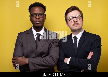 Zwei junge schöne afrikanische und kaukasische Männer posieren auf isoliertem gelben Hintergrund. Portrait von stilvollen selbstbewussten Mann in formelle Kleidung. Stockfoto