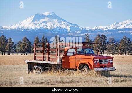 Ein uralter roter Farmwagen auf einem Feld unterhalb des South Sisters Peak in den Oregon Cascade Mountains in der Nähe des kleinen Ferienortes Sisters, Oregon. Stockfoto
