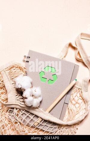 Netzbeutel und wiederverwendbarer Notizblock mit grünem Recycling-Zeichen auf beigem Hintergrund. Zero Waste und nachhaltiges Lifestyle-Konzept. Stockfoto