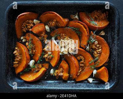 Gerösteter Orangenkürbis mit Knoblauch und Thymian auf schwarzer Backform. Dunkler Hintergrund. Overhead-Aufnahme. Stockfoto