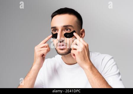 Junger hispanischer Mann, der Augenflecken isoliert auf Grau anwendet Stockfoto