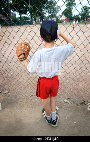 6 Jahre alt Junge Uhren Baseball T Ball Little League Aktion hinter einem Zaun Stockfoto