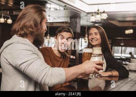 Schöner junger Mann, der fröhlich lächelt und sich mit seinen Freunden an der Bar ausruhen kann. Eine Gruppe von Freunden, die im örtlichen Bierkneipe etwas trinken. Zwei Männer und sein Stockfoto