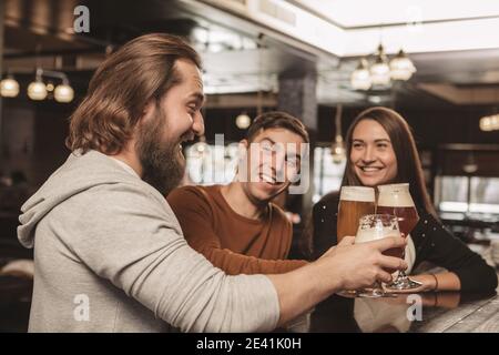 Eine Gruppe von glücklichen Freunden, die ihre Biergläser anklimmerten, fröhlich lachten und im irish Pub feierten. Bärtiger Mann, der aufgeregt schreit und mit Hallo rösten kann Stockfoto