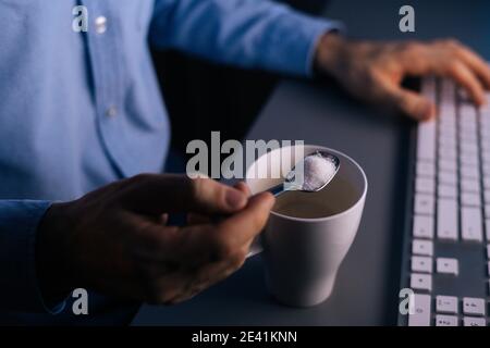 Nahaufnahme der Hände unkenntlich Mann Gießen Zucker auf Kaffee In Tasse mit kleinem Metalllöffel Stockfoto