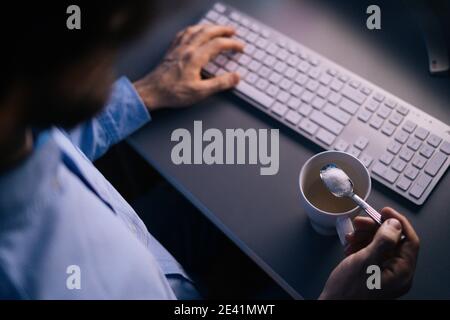 Draufsicht der Hände unkenntlich Mann Gießen Zucker auf Kaffee In Tasse mit kleinem Metalllöffel Stockfoto