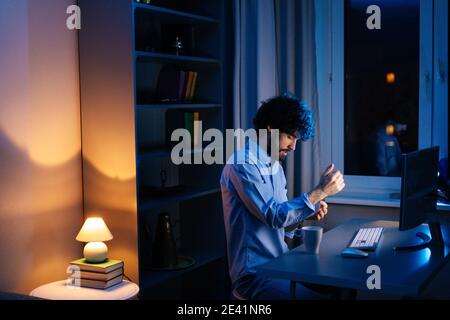 Seitenansicht des jungen Freiberuflers, der am Computer arbeitet und schreibt Text auf der kabellosen Tastatur spät in der Nacht Stockfoto