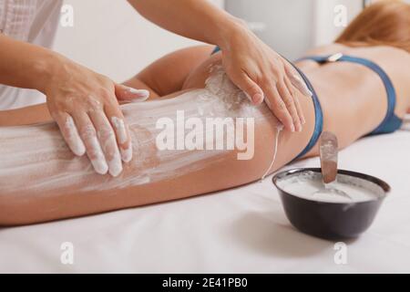 Ein kurzer Schuss eines professionellen Spa-Therapeuten, der weißen Schlamm auf den Körper einer jungen Frau aufführt. Nicht erkennbare Frau, die Körperpackung bei sp Stockfoto