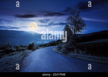 Landstraße in den Bergen in der Nacht. Schöne Aussicht in die Ferne nebligen Tal von der Spitze des Passes. Bäume entlang des Weges in Vollmondlicht Stockfoto